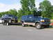 1995 Ford C-350 (Centurion Conversions) - A dark blue Ford Bronco is loaded onto a trailer, being towed by a dark green Ford F-Series SUV.