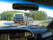 1995 Ford C-350 (Centurion Conversions) - A lifted blue Ford Bronco is towed on a trailer, with another dark SUV visible on the road ahead.