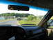 1995 Ford C-350 (Centurion Conversions) - A truck tows a car on a trailer down a road, seen from the perspective of the towing vehicle's interior.
