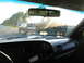 1995 Ford C-350 (Centurion Conversions) - View from inside a vehicle shows a truck towing a trailer carrying a large, lifted SUV on a highway.