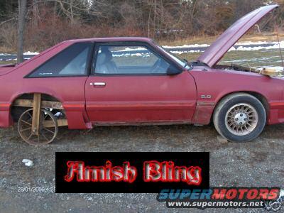 red Ford Mustang coupe, hood up, front wheel is standard, rear is replaced with wooden cart wheel