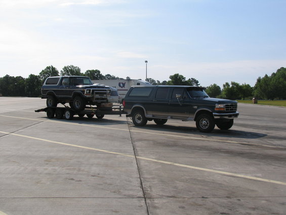 Dark green Ford Bronco on trailer towed by dark green Ford F-Series truck, 3q-front view