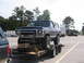 1995 Ford C-350 (Centurion Conversions) - A dark blue Ford Bronco is loaded onto a trailer, ready for transport.