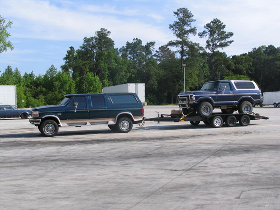 Dark green 1992 Ford F-250/350 Super Duty pickup truck towing a blue Ford Bronco on a triple-axle trailer