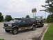 1995 Ford C-350 (Centurion Conversions) - A 1995 Ford C-350 Centurion Conversion is seen towing a pickup truck on a trailer near a steakhouse.