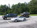 1995 Ford C-350 (Centurion Conversions) - A dark blue Ford Bronco is loaded onto a trailer, parked alongside a green Ford SUV and a silver convertible.