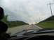 1995 Ford C-350 (Centurion Conversions) - Driving on a highway with a cloudy sky and trees lining the road. Another car is visible ahead.