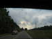 1995 Ford C-350 (Centurion Conversions) - A red pickup truck travels down a two-lane highway on an overcast day.