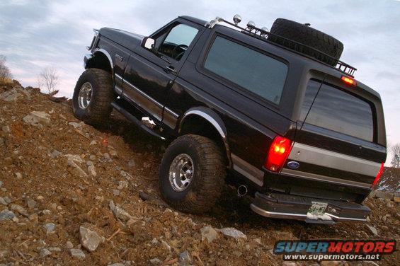 Black 1995 Ford Bronco climbing a dirt hill, spare tire on roof rack