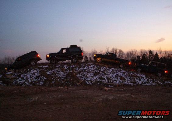 Bronco, pickup truck, and two SUVs on a snowy dirt hill at dusk