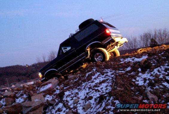 Black 1995 Ford Bronco climbing a rocky, snow-dusted hill at dusk