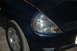 2002 Ford Coupe - Close-up of the front corner of a dark blue hatchback, highlighting the headlight assembly and front tire.