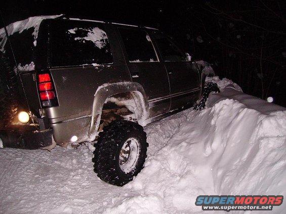 Brown SUV with large tires stuck in a snowdrift at night