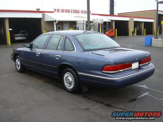Blue sedan parked at a car wash. Another car is visible inside one of the wash bays
