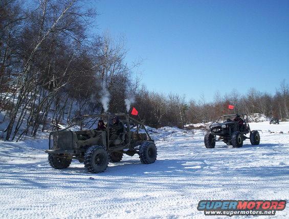 Two off-road vehicles with exhaust smoke in a snowy landscape with trees