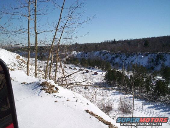 Several red SUVs parked in a snow-covered field with trees and a quarry in the background