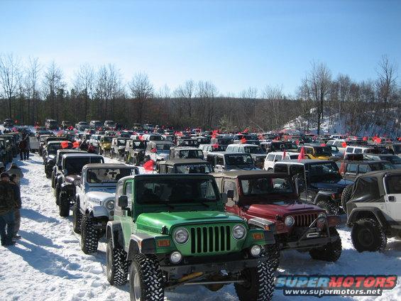 Green 2002 Jeep Wrangler in foreground, many other Jeeps parked in snow behind it