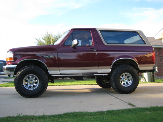 Maroon 1996 Ford Bronco with tan top, lifted suspension, and aftermarket wheels parked on a driveway