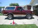 1996 Ford Bronco - A maroon 1996 Ford Bronco with a tan removable top is parked in a driveway with a jack and car parts nearby.