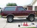 1996 Ford Bronco - A maroon and tan 1996 Ford Bronco is parked on a driveway with its suspension lifted.