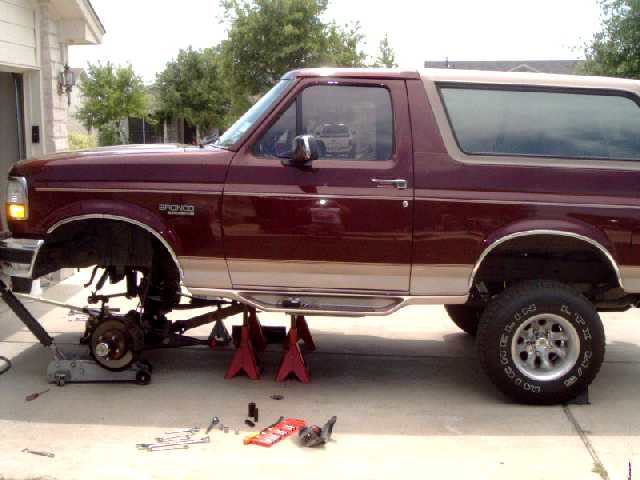 Maroon 1996 Ford Bronco on jack stands with front suspension disassembled. Tools are on the ground