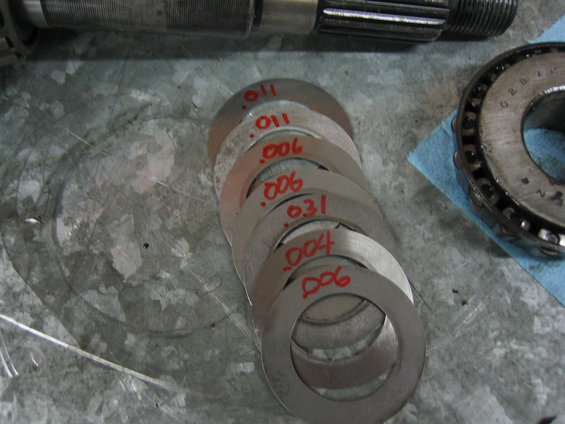 Stack of metal shims marked with thicknesses like .011, .006, .004, and .031 next to a bearing