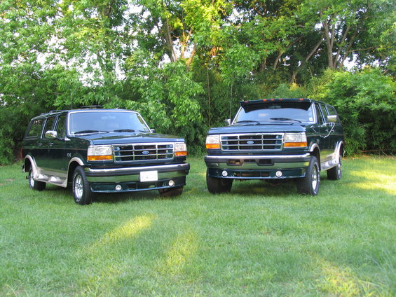 Two dark green Ford Broncos parked on grass with trees in background