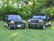 1995 Ford C-350 (Centurion Conversions) - Two Ford Bronco SUVs are parked side-by-side on a grassy lawn with trees in the background.