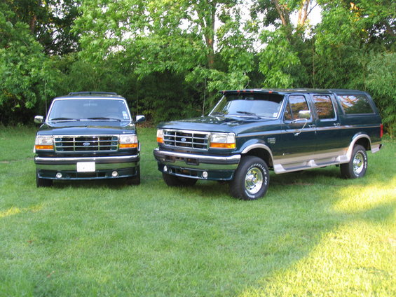 Two dark green Ford SUVs parked on grass. The one on the right is a Centurion Conversion. The one on the left is a Ford Bronco