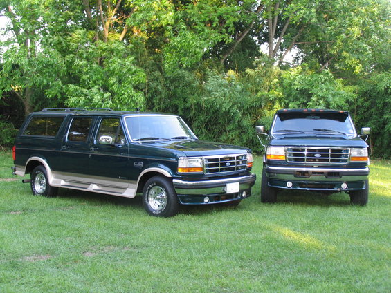 Two dark green Ford SUVs with tan trim parked on grass, one in front of the other