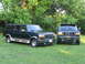 1995 Ford C-350 (Centurion Conversions) - Two dark green Ford SUVs with tan trim are parked on a grassy lawn with trees in the background.