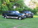 1995 Ford C-350 (Centurion Conversions) - Two Ford Bronco SUVs are parked side-by-side on a grassy lawn with trees in the background.