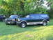 1995 Ford C-350 (Centurion Conversions) - Two Ford trucks, one a Centurion conversion SUV, are parked on a grassy area with trees in the background.