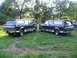 1995 Ford C-350 (Centurion Conversions) - Two dark green Ford Bronco Centurion Conversion SUVs are parked on a grassy lawn with trees in the background.