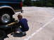 1995 Ford C-350 (Centurion Conversions) - A man secures a dark green van with tan trim onto a trailer in a parking lot.