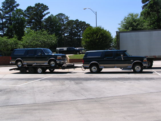 Dark green Ford Bronco SUV on a trailer, another similar SUV is parked next to it
