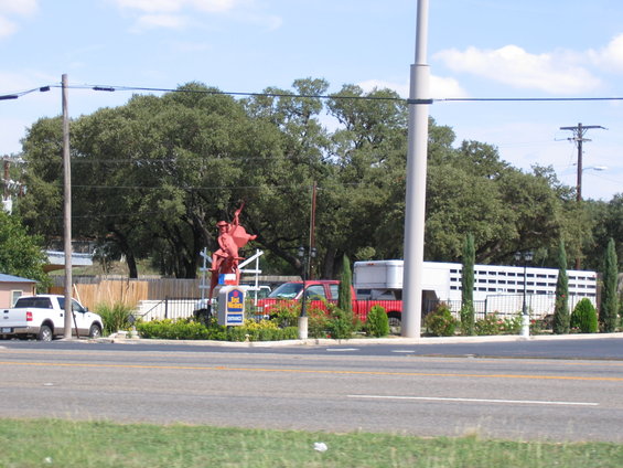 Red cowboy statue in front of a Best Western sign, with a white pickup truck, red truck, and white trailer
