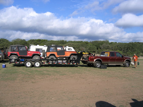 Red and orange Jeeps on a trailer pulled by a maroon pickup truck