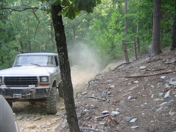 1979 Ford F-Series truck driving on a dirt trail, kicking up dust. Front grille and bumper are visible