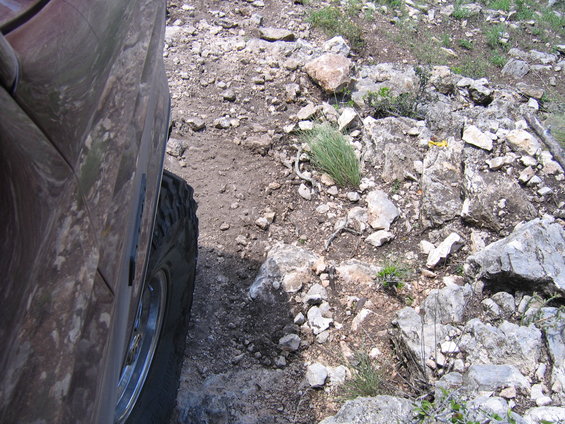 Side view of a muddy tire and fender of an off-road vehicle on a rocky trail