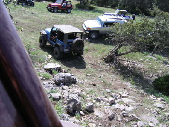 Blue Jeep Wrangler with soft top and spare tire on rear, parked on a grassy hill