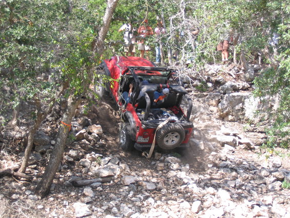 Red Jeep Wrangler with open top navigating rocky terrain, rear view