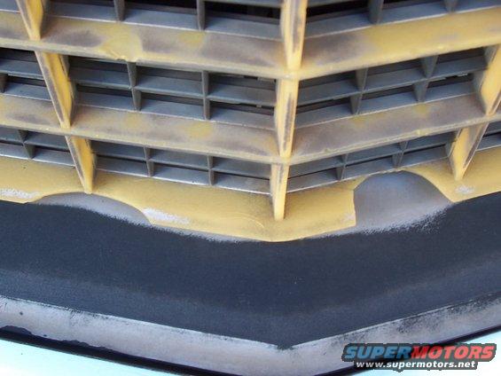 Close-up of a vehicle's front grille with yellow paint overspray on the gray plastic