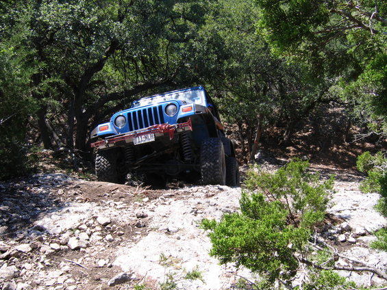 Blue Jeep Wrangler driving on a rocky, wooded trail