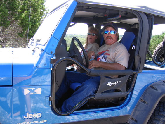 Blue Jeep Wrangler with two people inside, driver wearing sunglasses and a hat