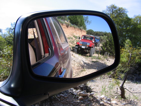 Red Jeep Wrangler on a dirt road, reflected in a side mirror