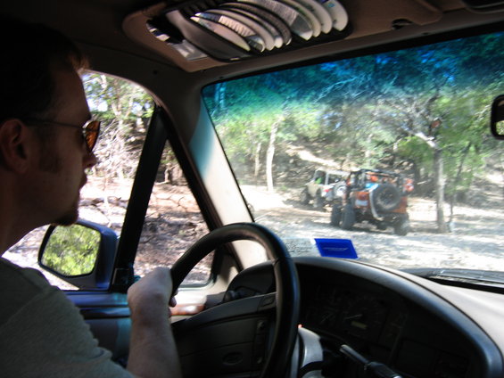 Interior view of a person driving an SUV on a dirt road with other off-road vehicles in the background