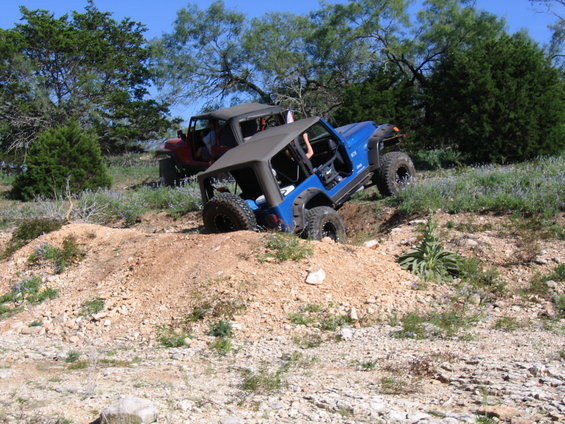Blue Jeep partially in a ditch with red Jeep behind it on a dirt trail