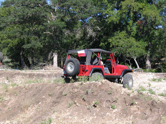 Red Jeep Wrangler with spare tire on back, driving on dirt mound