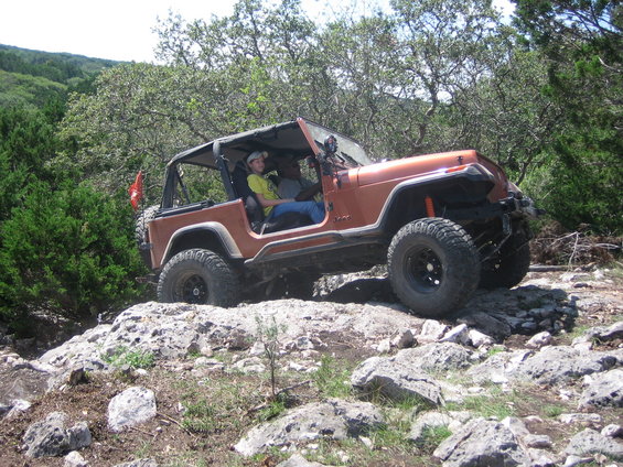 Orange Jeep Wrangler off-roading on rocks, with two people inside